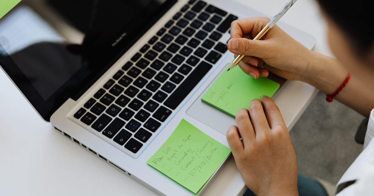 Mãos escrevendo notas em post-its ao lado de laptop