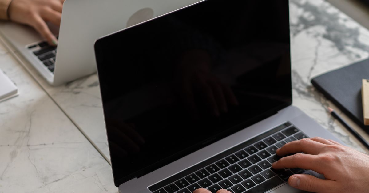 Duas pessoas trabalhando em notebooks numa mesa de mármore