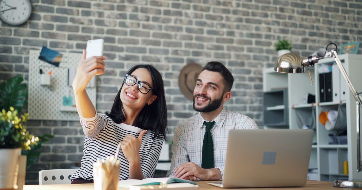 Colegas de trabalho sorrindo enquanto gravam selfie no escritório