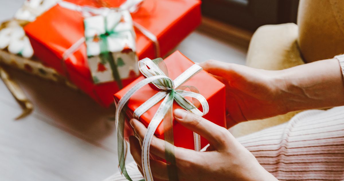 Mãos segurando uma caixa de presente vermelha com fita decorativa