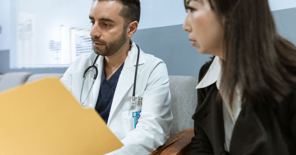 Médico de jaleco analisando documentos ao lado de uma mulher