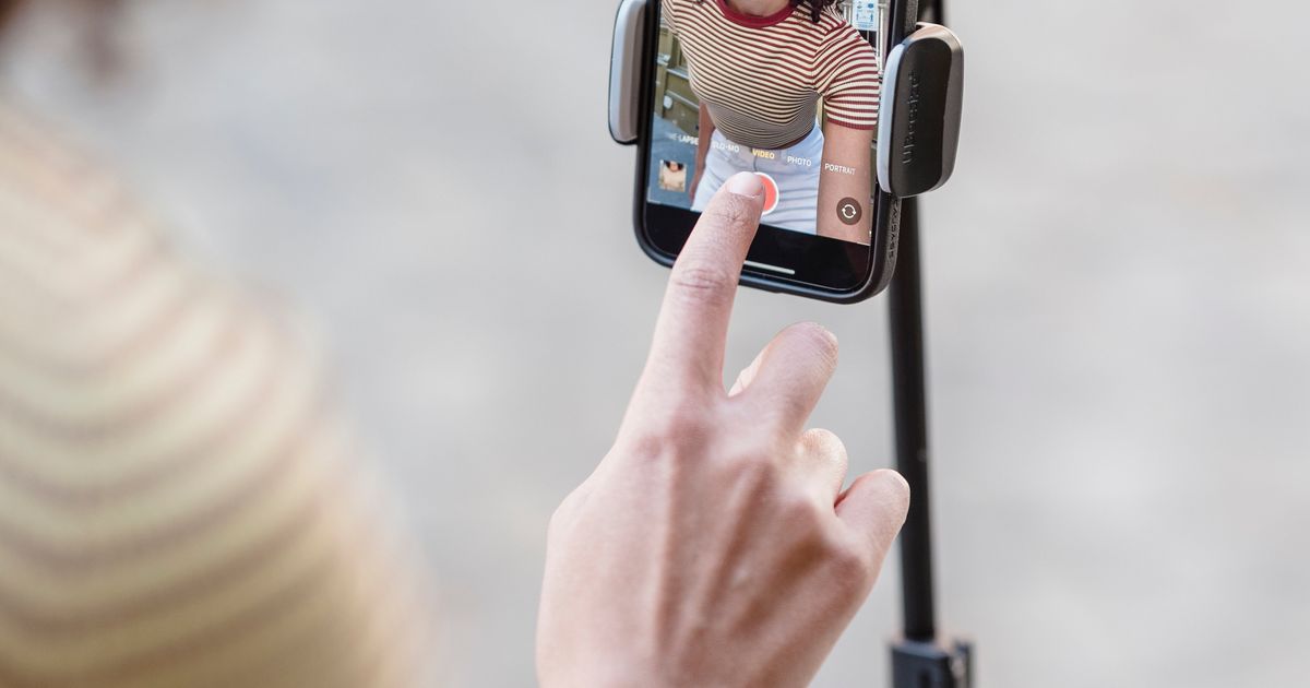 Mulher tocando o botão de gravar em um celular montado no tripé