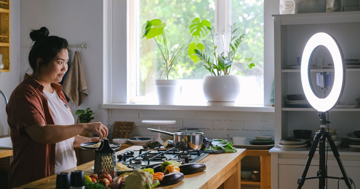 Criadora de conteúdo cozinhando em casa enquanto grava com celular e ring light no tripé