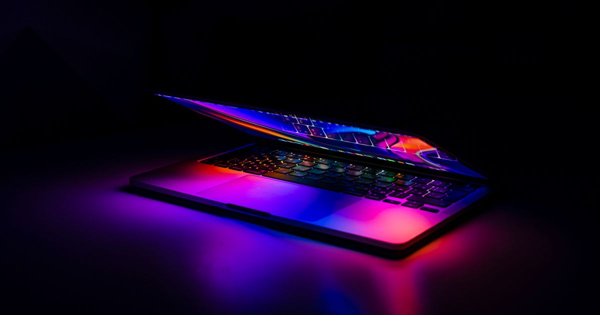Notebook quase fechado no escuro, com luzes coloridas refletidas no teclado