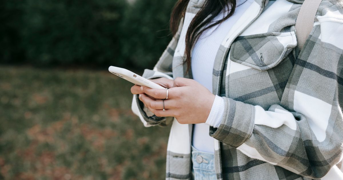 Mulher de camisa xadrez mexendo no celular ao ar livre