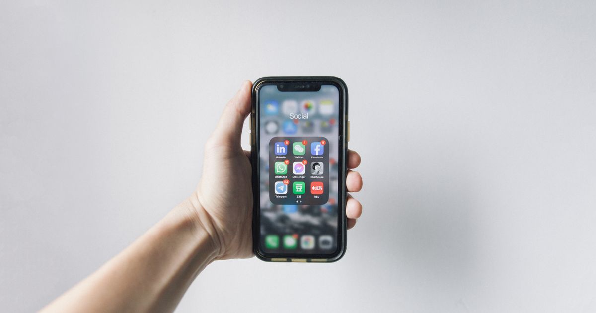 Mão segurando celular com pasta de aplicativos de redes sociais na tela